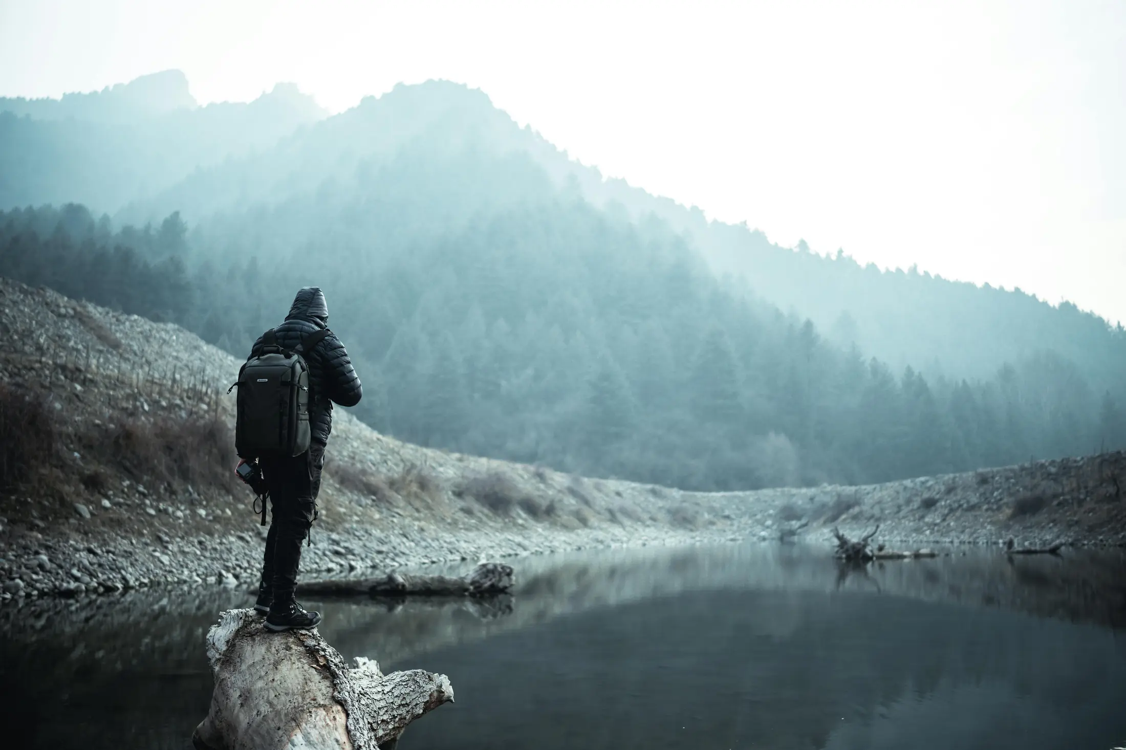 Randonneur sur un lac brumeux, montagnes et forêt en arrière-plan